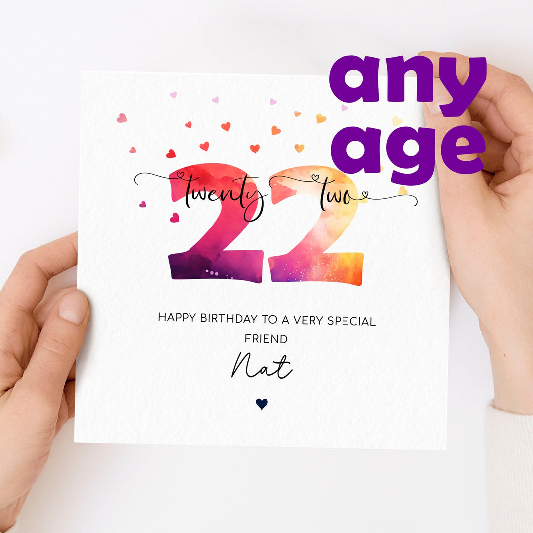 birthday card with bright and colourful ombre numbers in red, purple and yellow tones surrounded by many small hearts, and age written in words over it