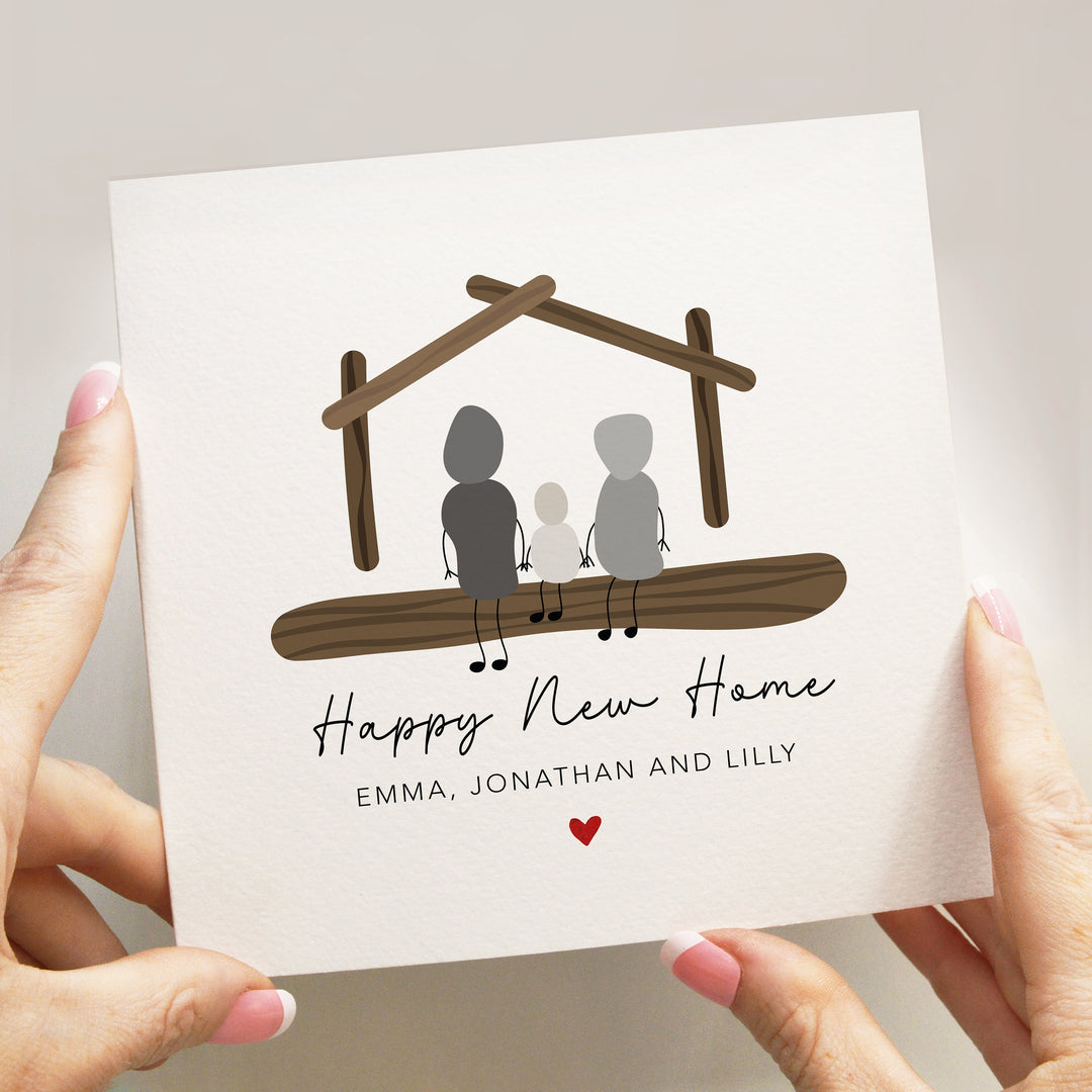 personalised cute congratulations on your 
new home happy new home
card with handwritten font and red heart and wood house and pebble people family of three sitting on a log in front of it